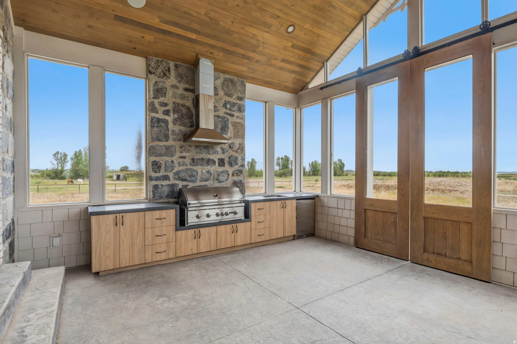 Outdoor kitchen featuring a built-in grill, stone accent wall, and wood-finish cabinetry with dark countertops