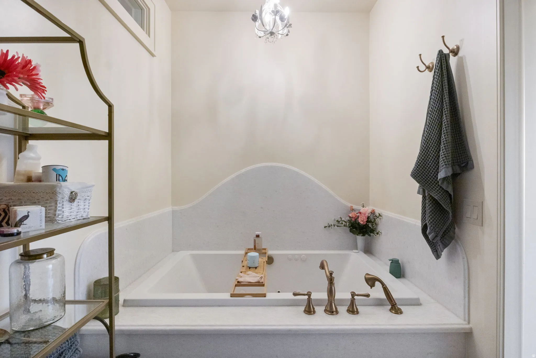 Soaking tub with bronze-finish fixtures, a decorative curved tile surround, and an overhead crystal-style light fixture