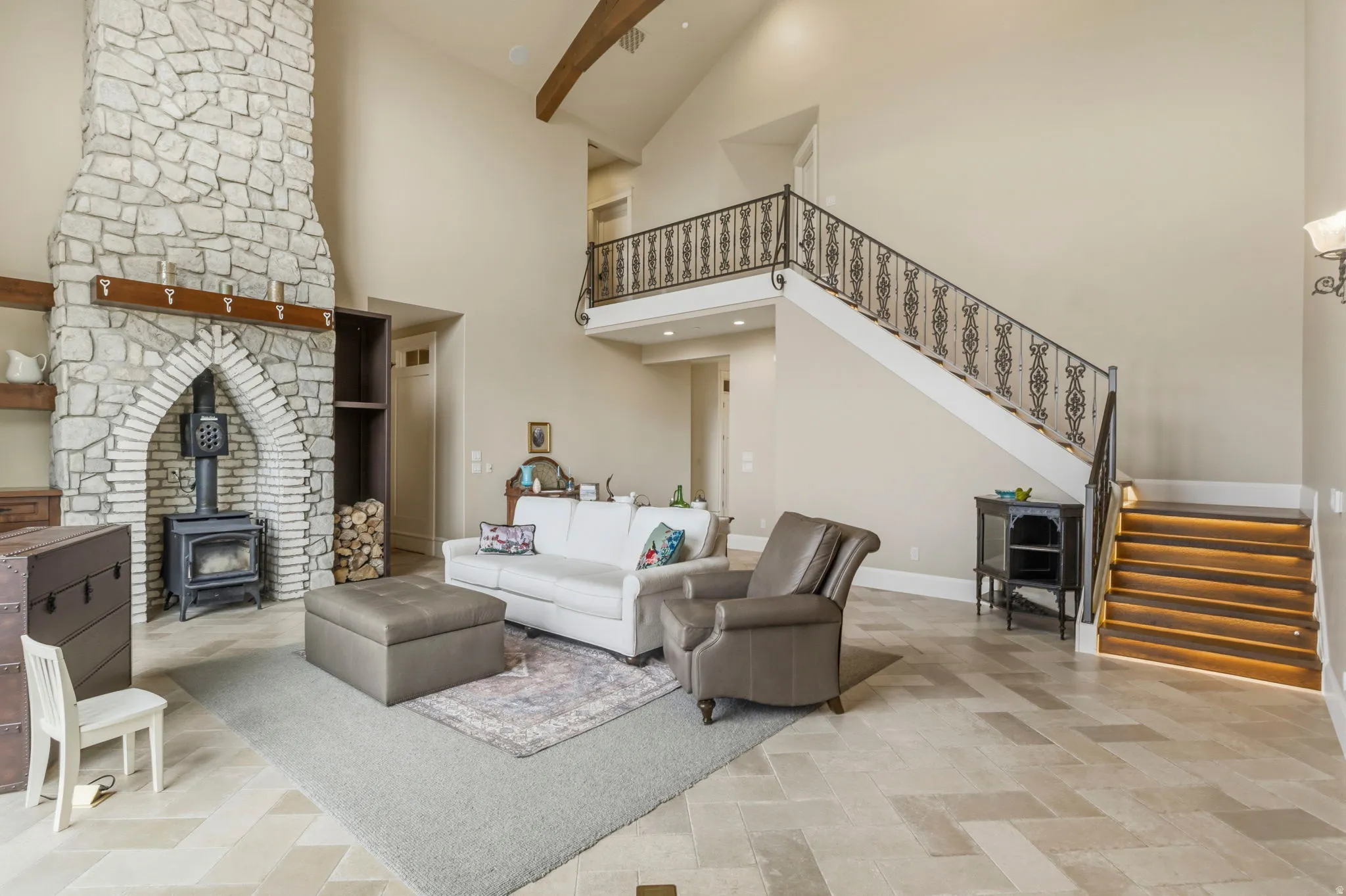 Great room featuring a prominent stone fireplace with a wood-burning stove insert, high vaulted ceilings, and light-toned tile flooring in a herringbone pattern