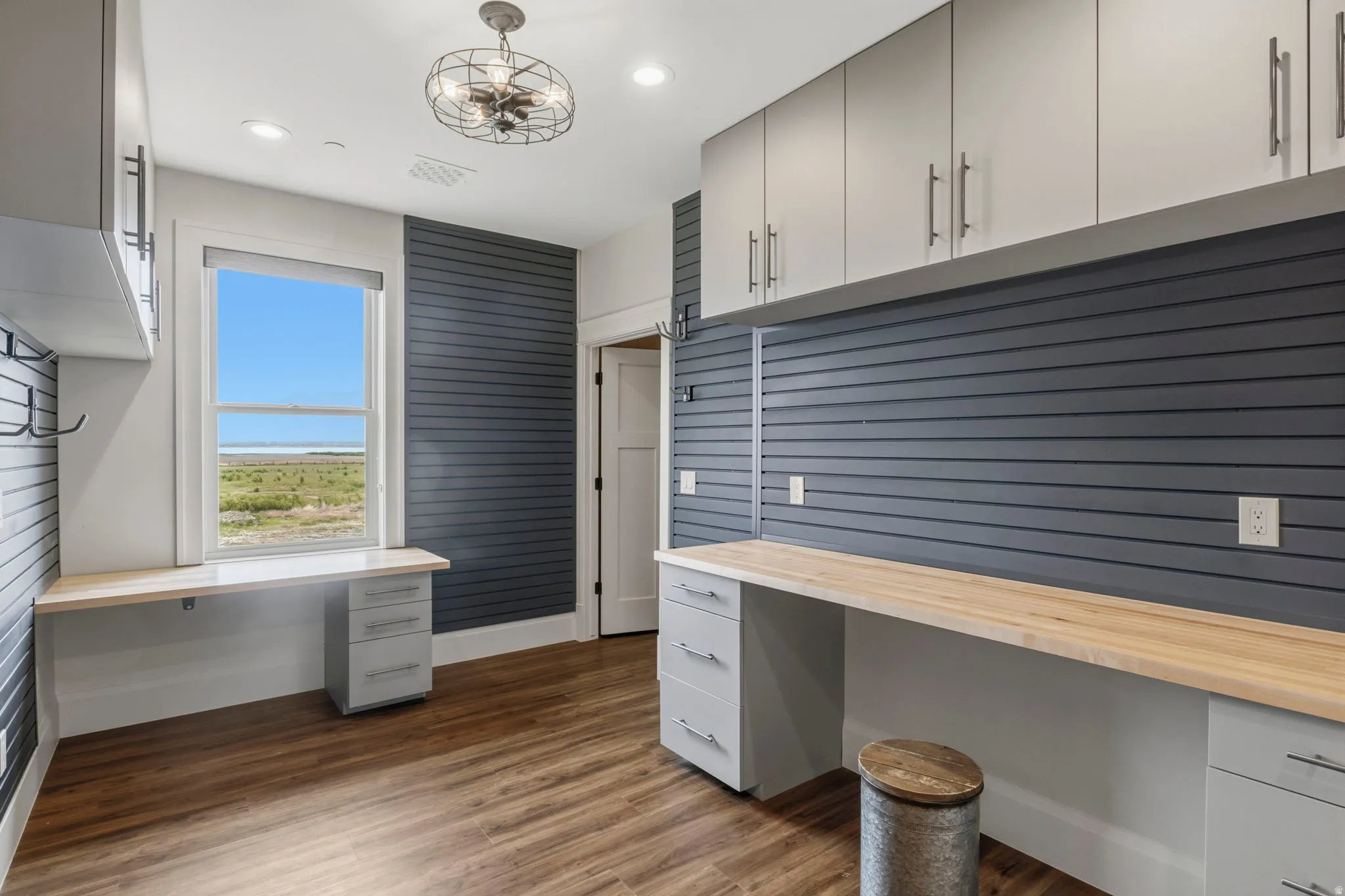 Hidden Workshop. Functional workspace featuring extensive built-in cabinetry, durable wood-finish flooring, and a window providing natural light