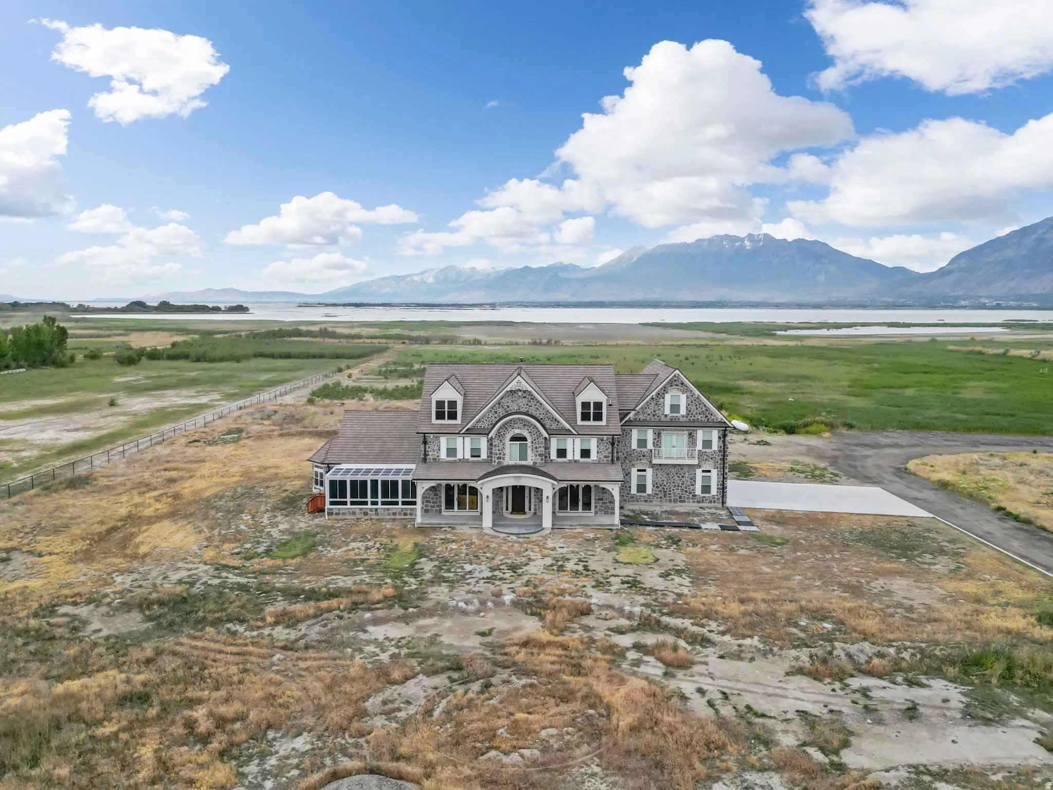 Grand stone and shingle-sided residence showcasing multiple dormers, an enclosed sunroom, and a prominent arched entryway