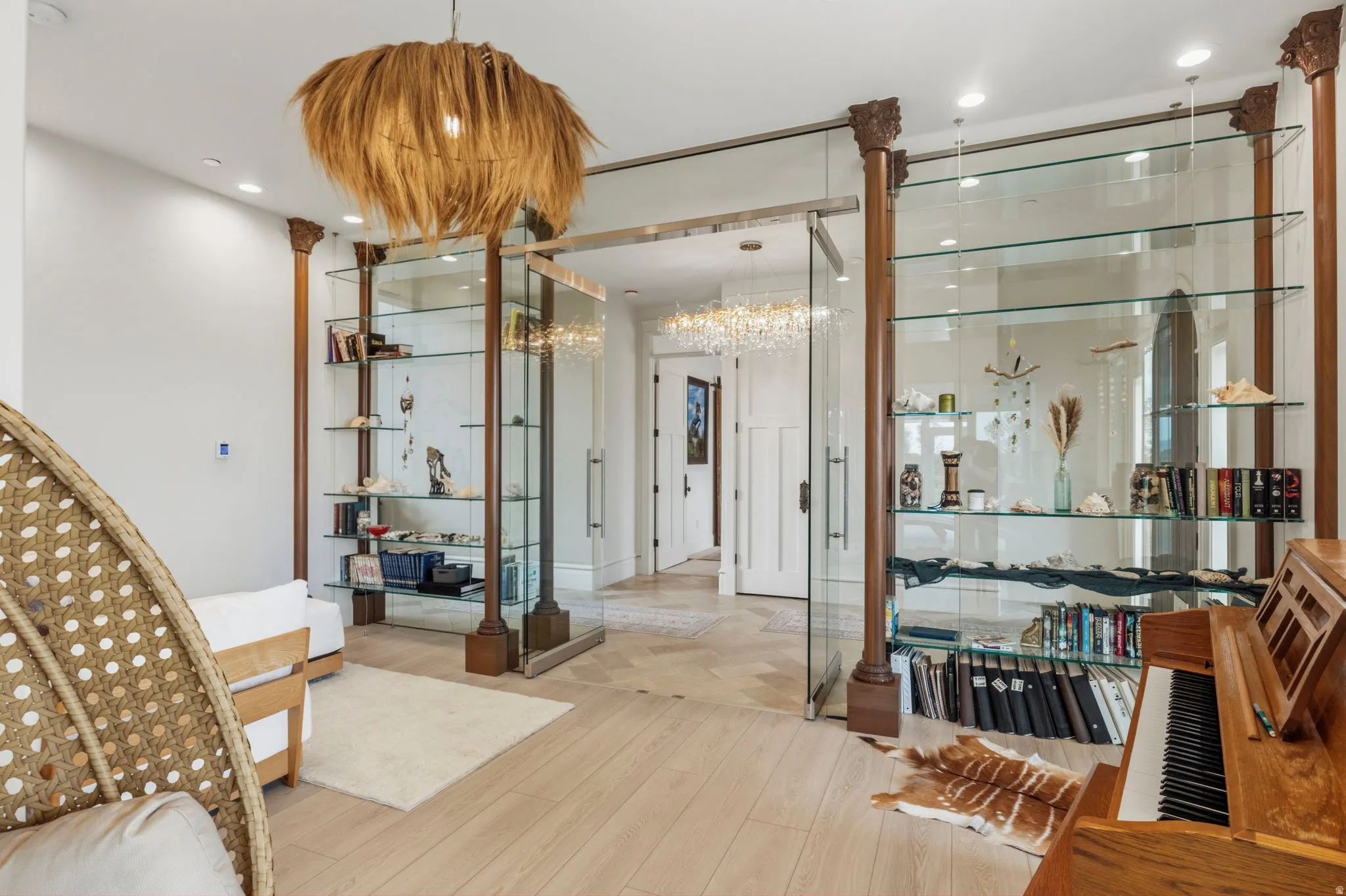 Room featuring wood-finish flooring, a decorative pendant light fixture, and built-in glass shelving units with architectural columns