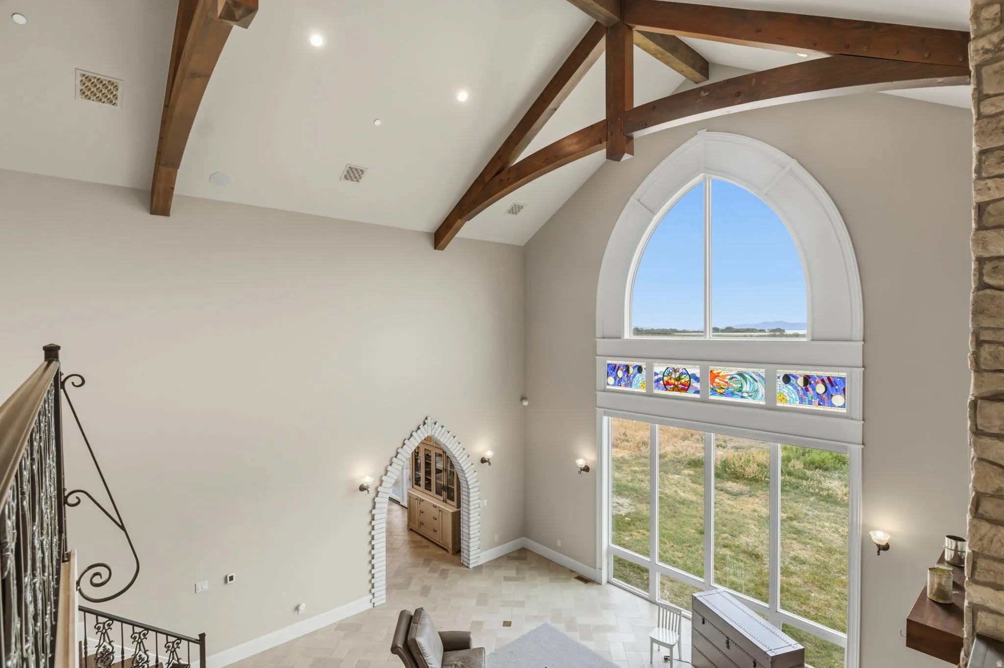 Vaulted ceiling with exposed wood beams, large arched window, and custom stained glass panels