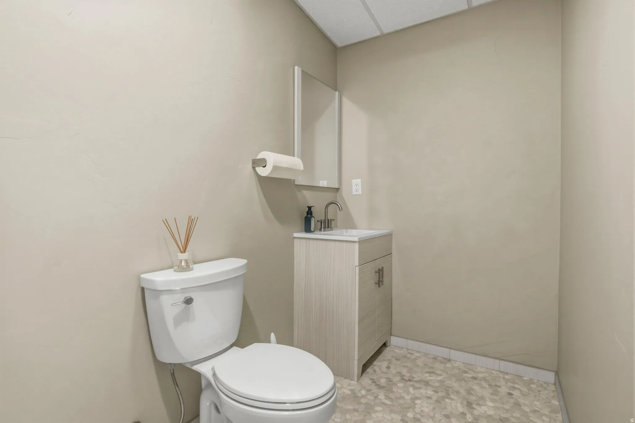 Compact powder room off the yoga studio featuring a toilet, vanity with integrated sink, wall-mounted mirror, and patterned flooring
