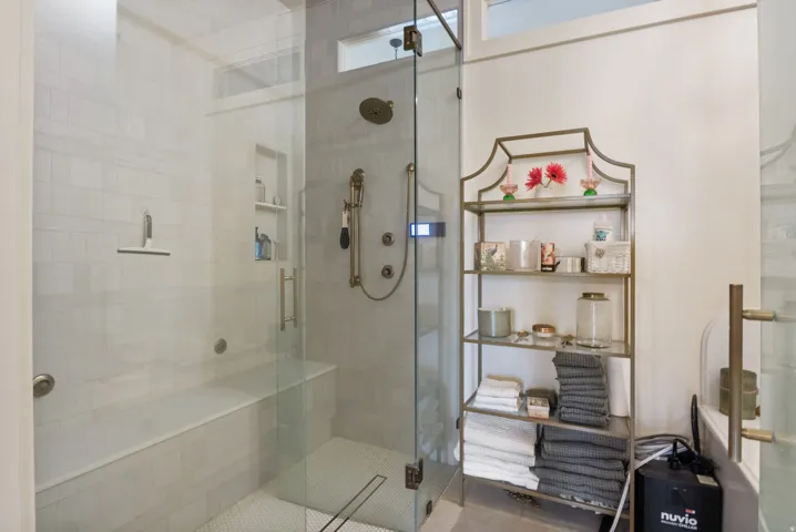 Walk-in shower featuring a glass enclosure, built-in bench, recessed shelf, and multiple shower heads