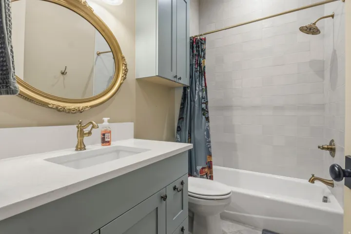 Bathroom featuring a light blue vanity with a white countertop and integrated sink, an ornate gold-framed mirror, a bathtub with subway tile surround, and coordinating brass fixtures