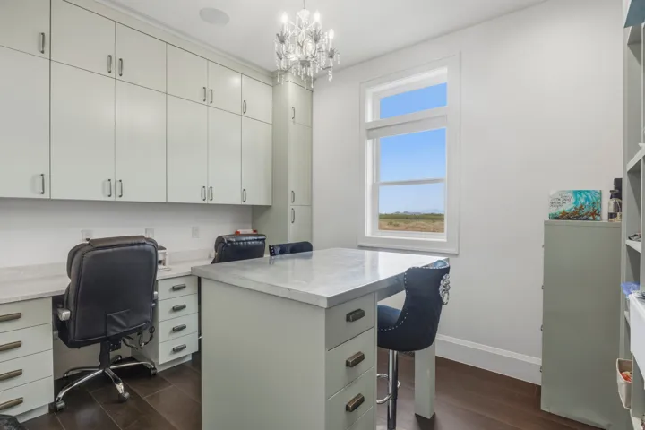 Craft room or Dedicated workspace featuring extensive built-in cabinetry, dual workstations with light-toned countertops, a central island with a contrasting countertop, and dark wood-finish flooring