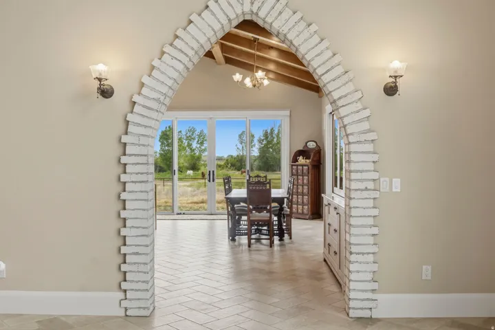 Brick archway entry to Kitchen featuring sconce lighting, herringbone flooring, vaulted ceiling with exposed beams, and sliding glass doors to outdoor spaces