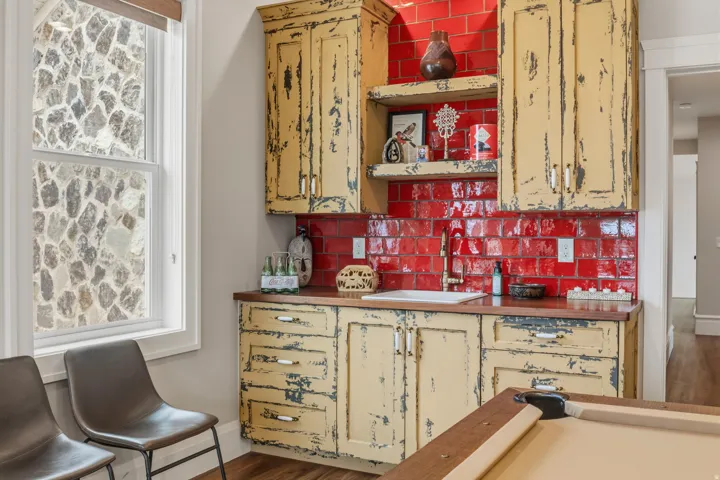 Wet bar featuring distressed cabinetry, a red subway tile backsplash, and a built-in sink with a gold-toned faucet