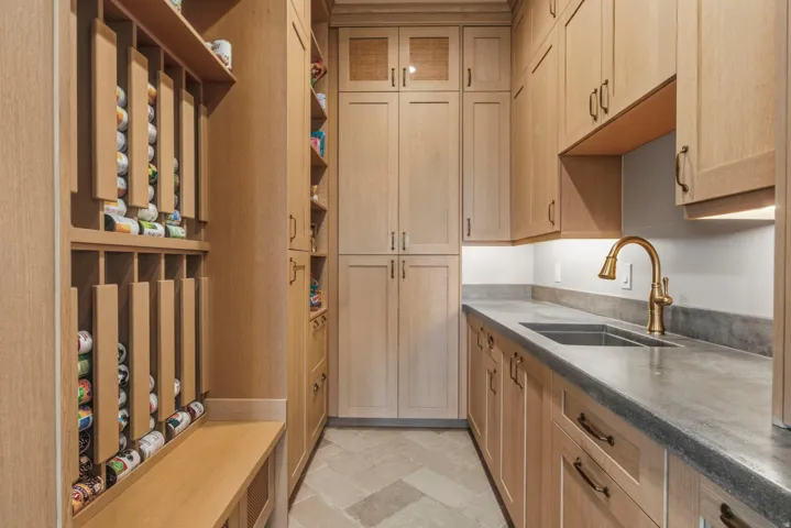 Custom pantry featuring light wood cabinetry, integrated roll-out storage, durable countertops, and an undermount sink with a bronze-finish faucet