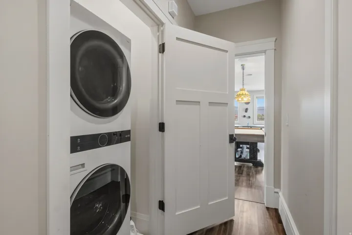 Stackable washer and dryer unit, white paneled interior door with dark hardware, light gray walls, and wood-finish flooring