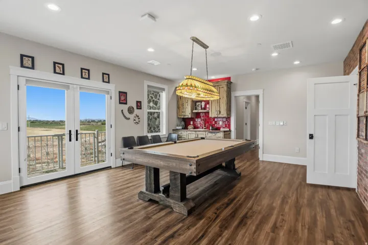 Spacious entertainment room featuring wood-finish flooring, a built-in wet bar with red tile backsplash, and recessed lighting