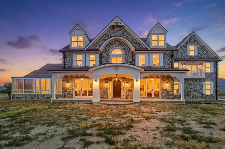 Stone-clad exterior featuring multiple dormers, a covered porch with white columns, and a sunroom extension