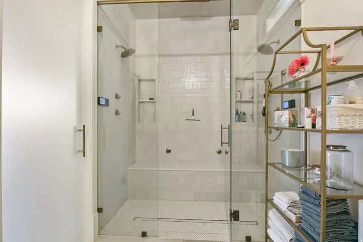 Spacious glass-enclosed shower with multiple shower heads, integrated bench seating, and recessed shelving