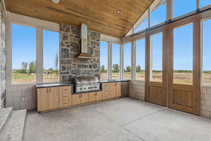 Outdoor kitchen featuring a built-in grill, stone accent wall, and wood-finish cabinetry with dark countertops