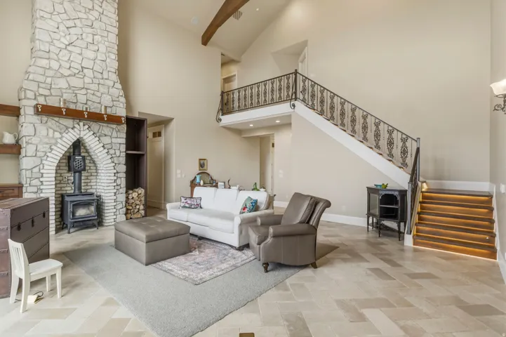 Great room featuring a prominent stone fireplace with a wood-burning stove insert, high vaulted ceilings, and light-toned tile flooring in a herringbone pattern