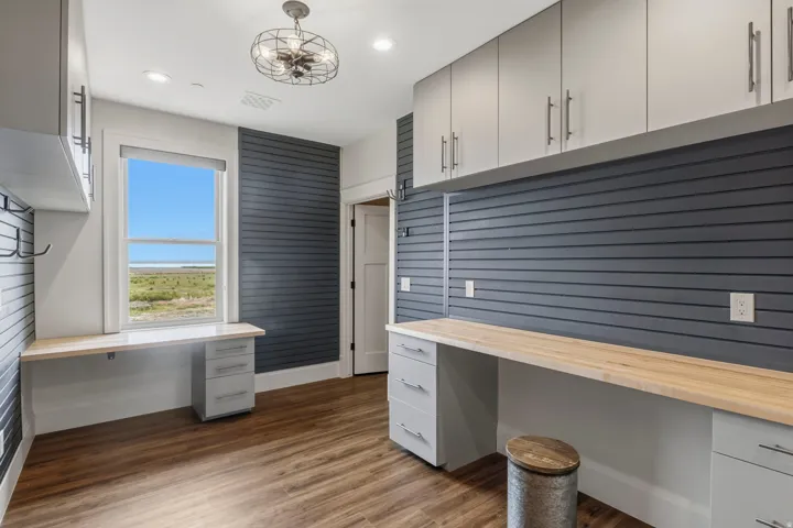 Hidden Workshop. Functional workspace featuring extensive built-in cabinetry, durable wood-finish flooring, and a window providing natural light