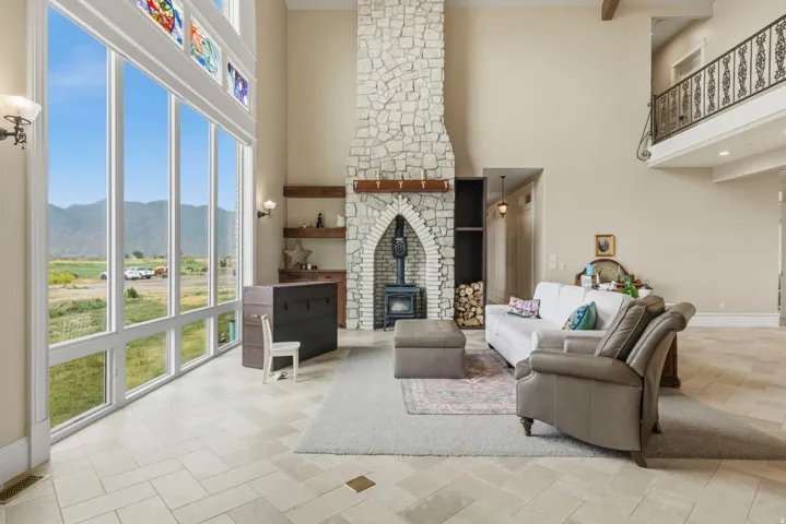 Spacious living area featuring floor-to-ceiling windows, a stone fireplace with a wood-burning stove, and a second-story balcony with decorative ironwork