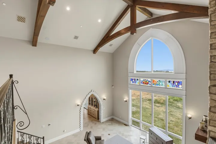 Vaulted ceiling with exposed wood beams, large arched window, and custom stained glass panels