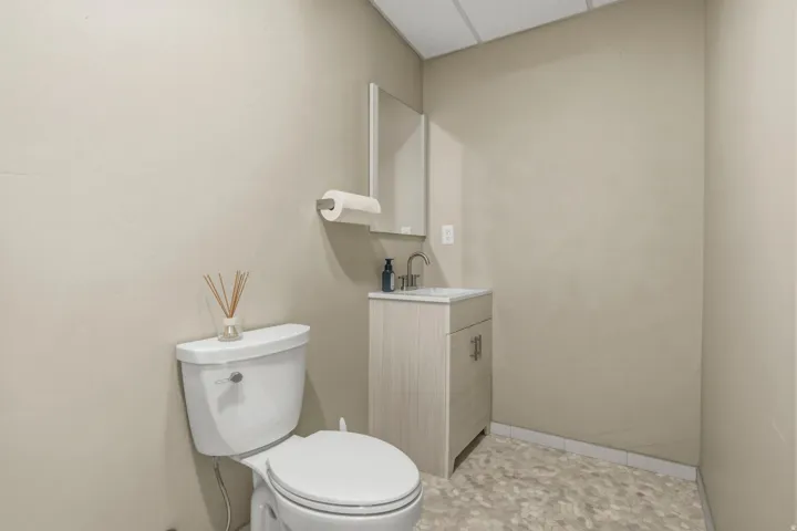 Compact powder room off the yoga studio featuring a toilet, vanity with integrated sink, wall-mounted mirror, and patterned flooring