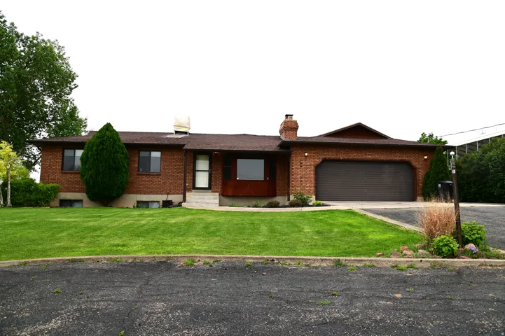 Brick facade residence featuring a two-car garage with a brown roll-up door, a front lawn, mature landscaping, and a multi-pane front door