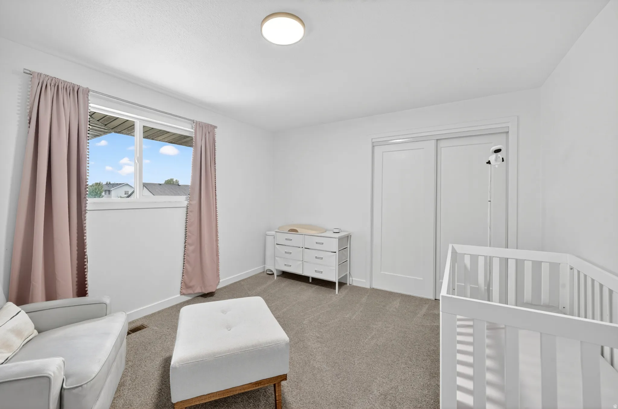 Light-filled room featuring a double window, neutral carpeting, white walls, a built-in sliding door closet, and a flush mount ceiling light