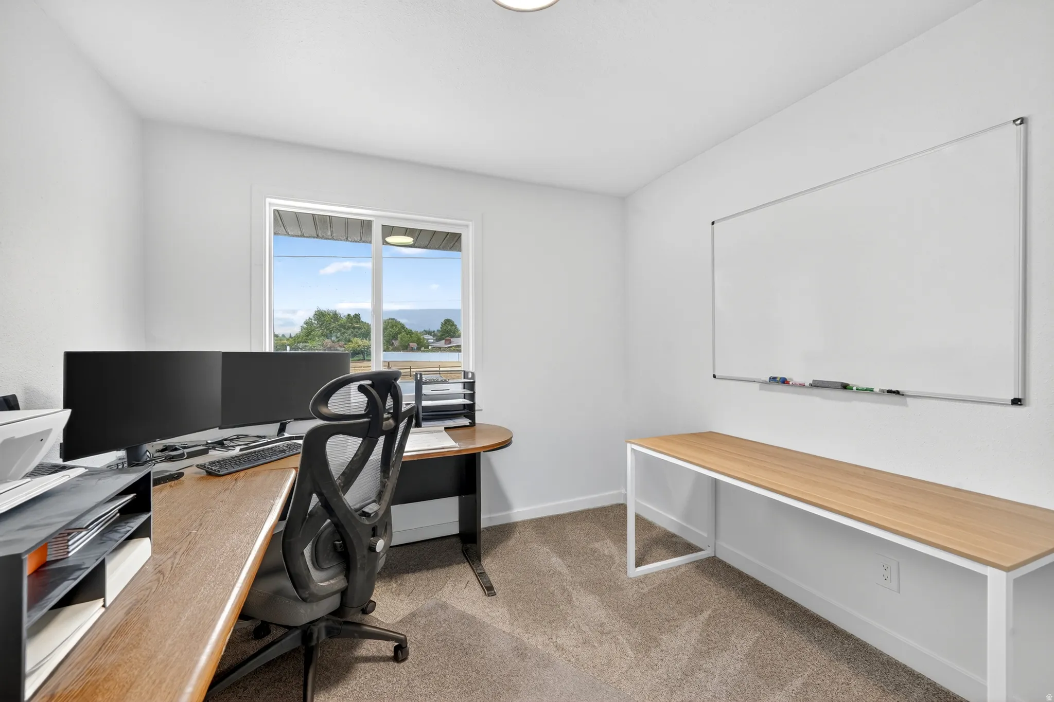 Spacious room featuring neutral carpet flooring, white walls, and a large window providing outdoor scenery