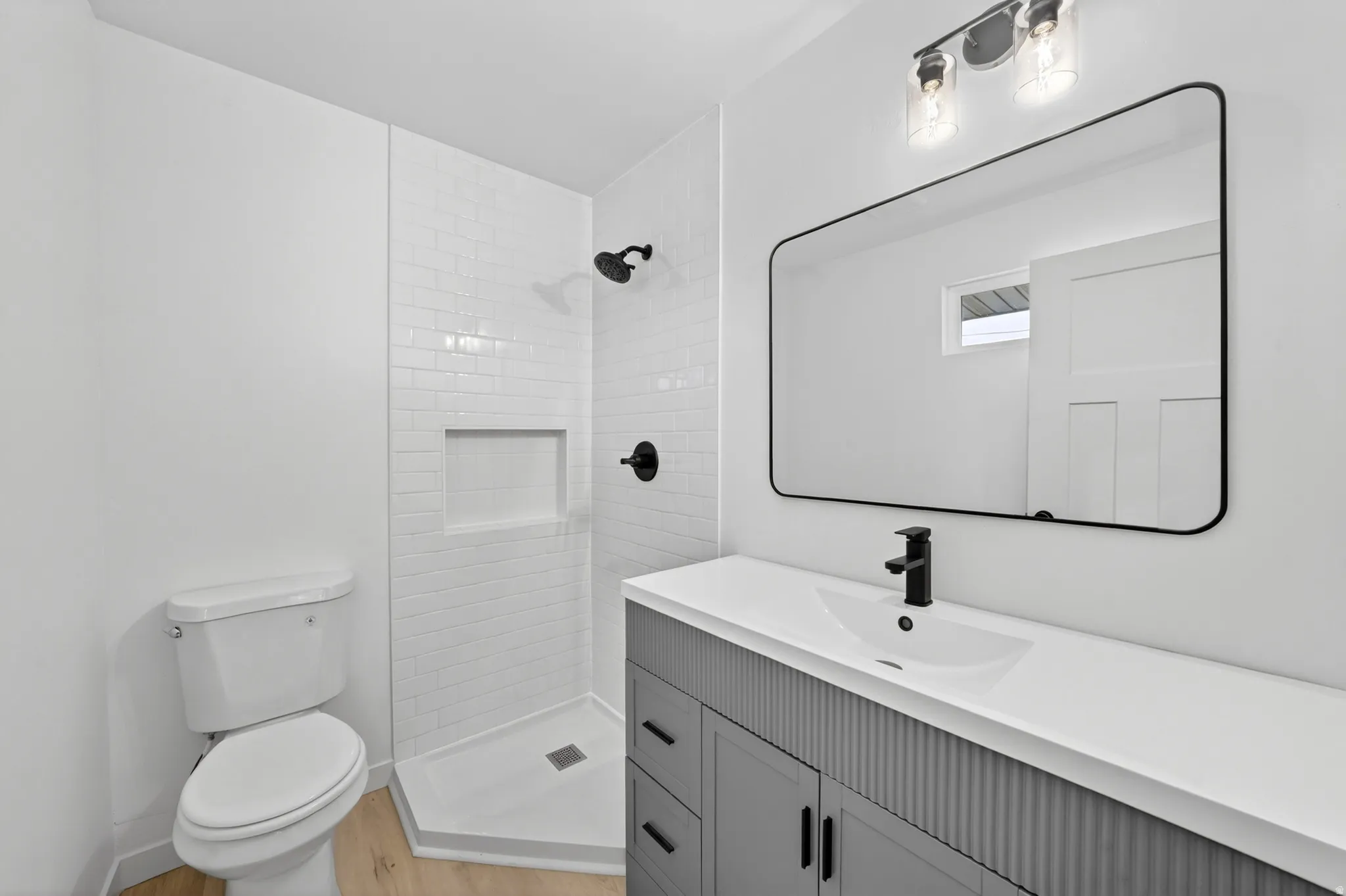 Bathroom featuring a gray fluted vanity with an integrated sink, black rectangular mirror, and a white subway tile shower with a recessed niche