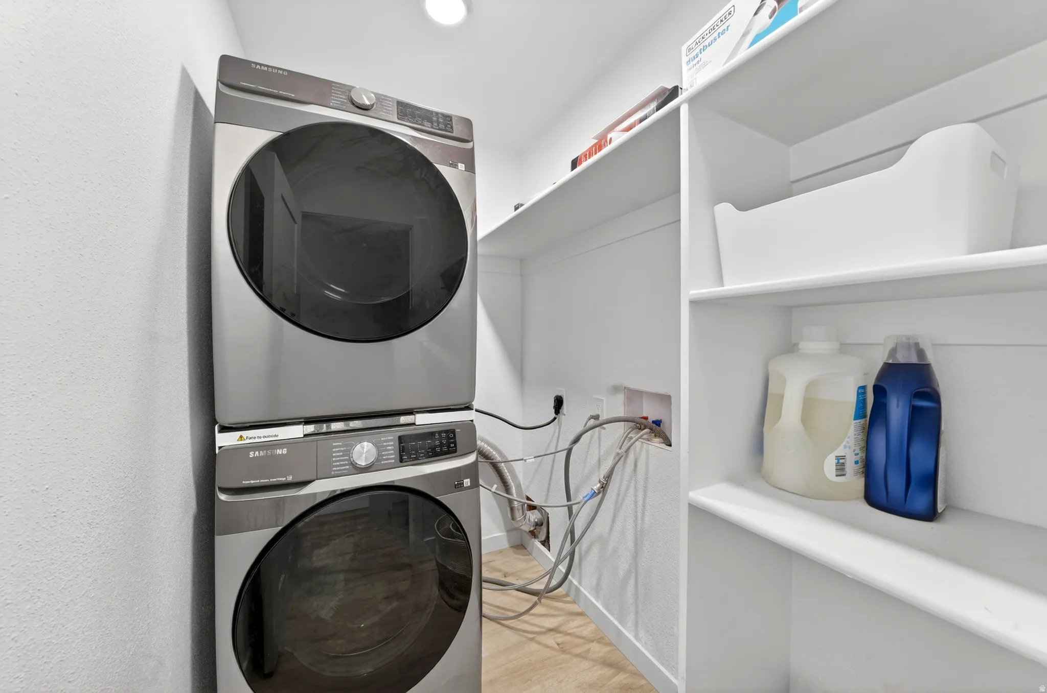 Dedicated laundry area featuring a stacked washer and dryer unit, multiple built-in shelving units, and light wood-finish flooring