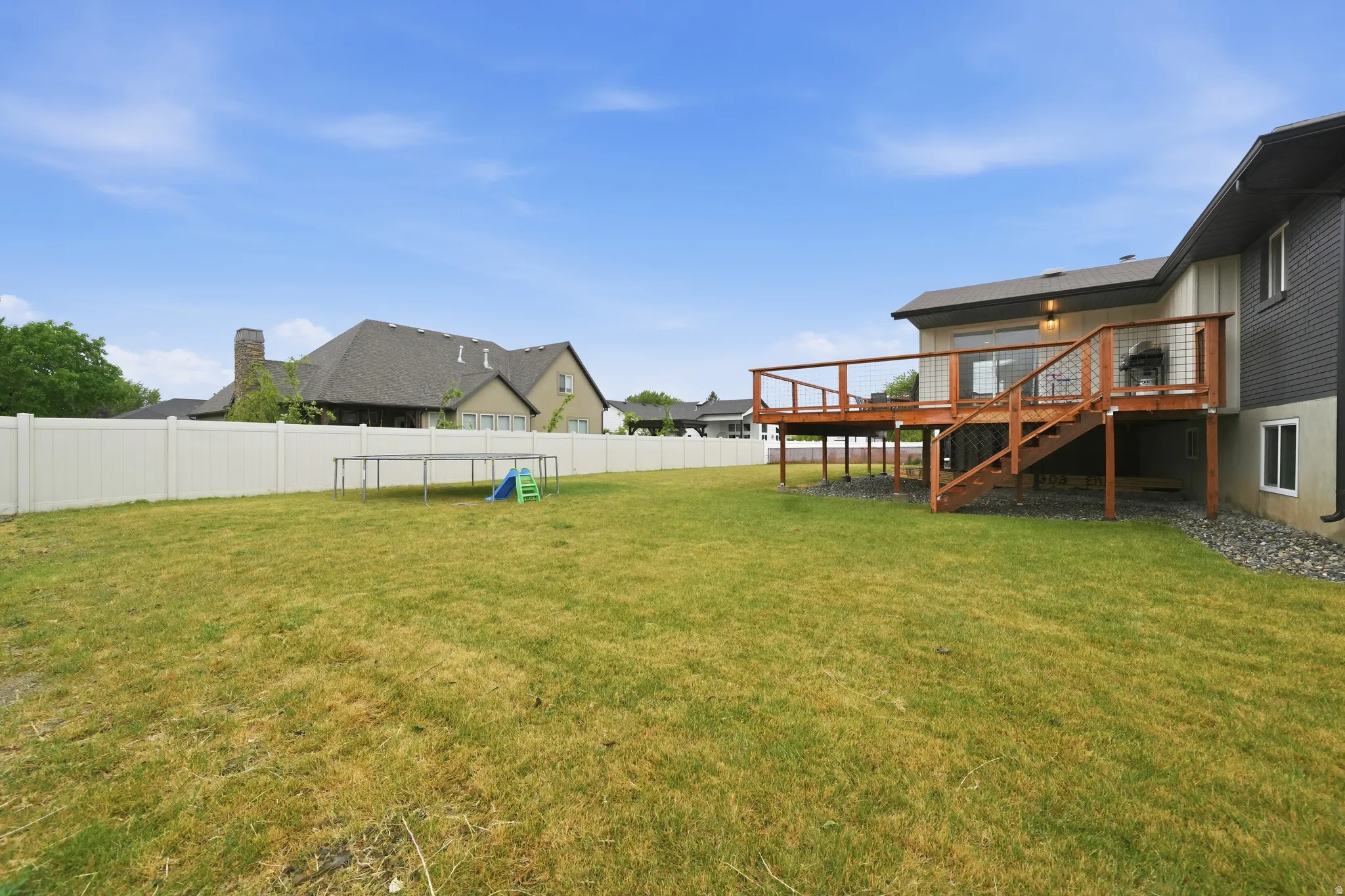 Expansive backyard featuring a green lawn, a privacy fence, and a multi-level wood deck with cable railings and stairs