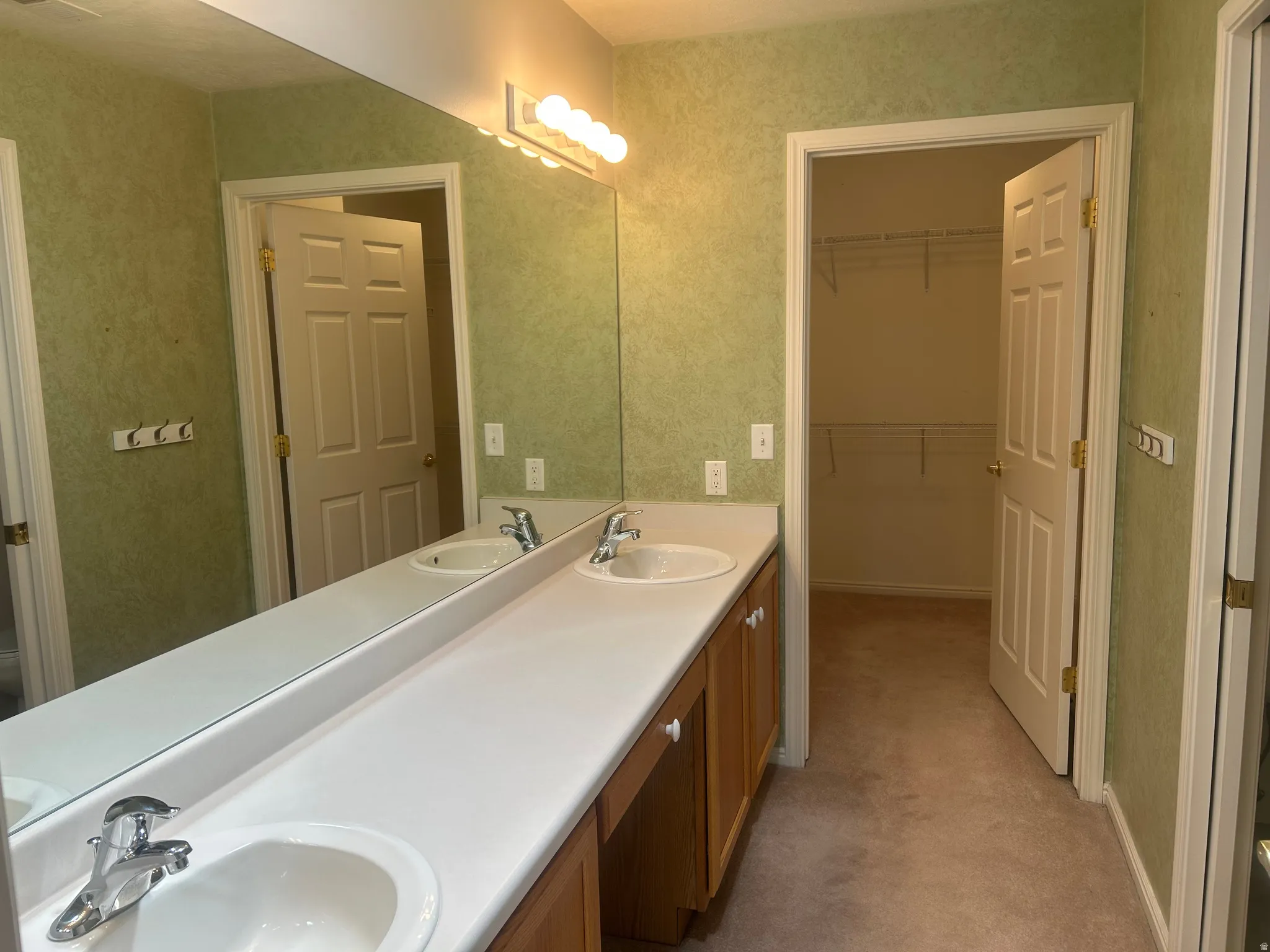 Primary bathroom vanity featuring dual sinks, a large mirror, and ample under-sink cabinetry