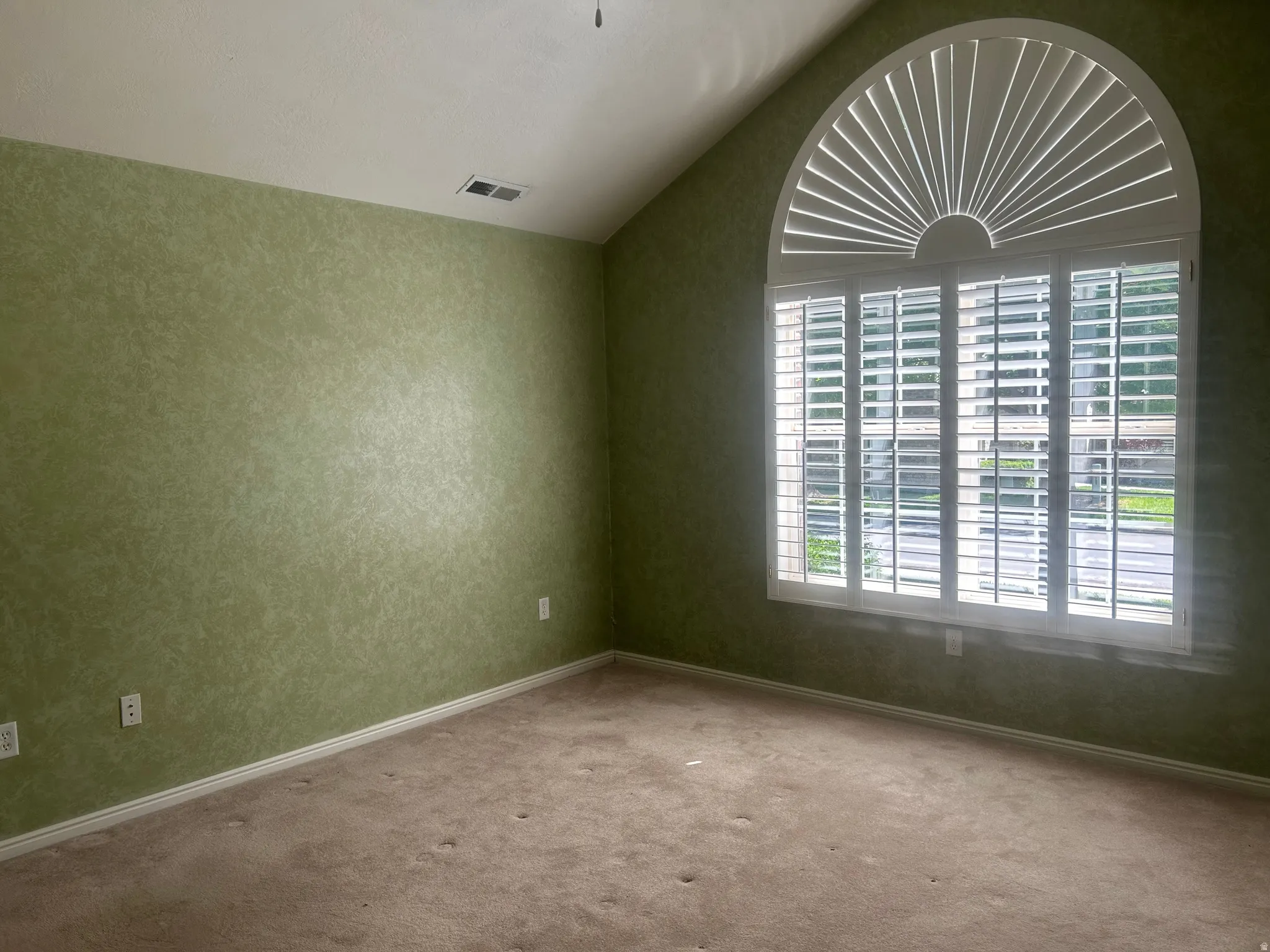 Primary bedroom with vaulted ceiling room featuring a large arched window with plantation shutters