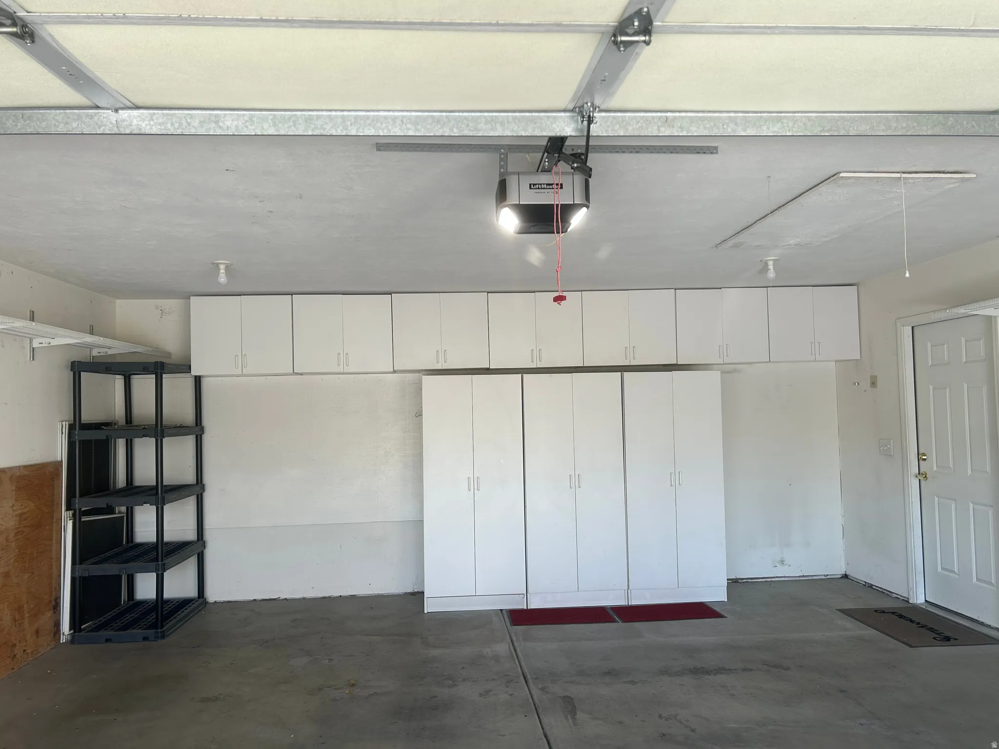 Garage with concrete flooring, overhead cabinetry, full-height storage cabinets, and a white interior door