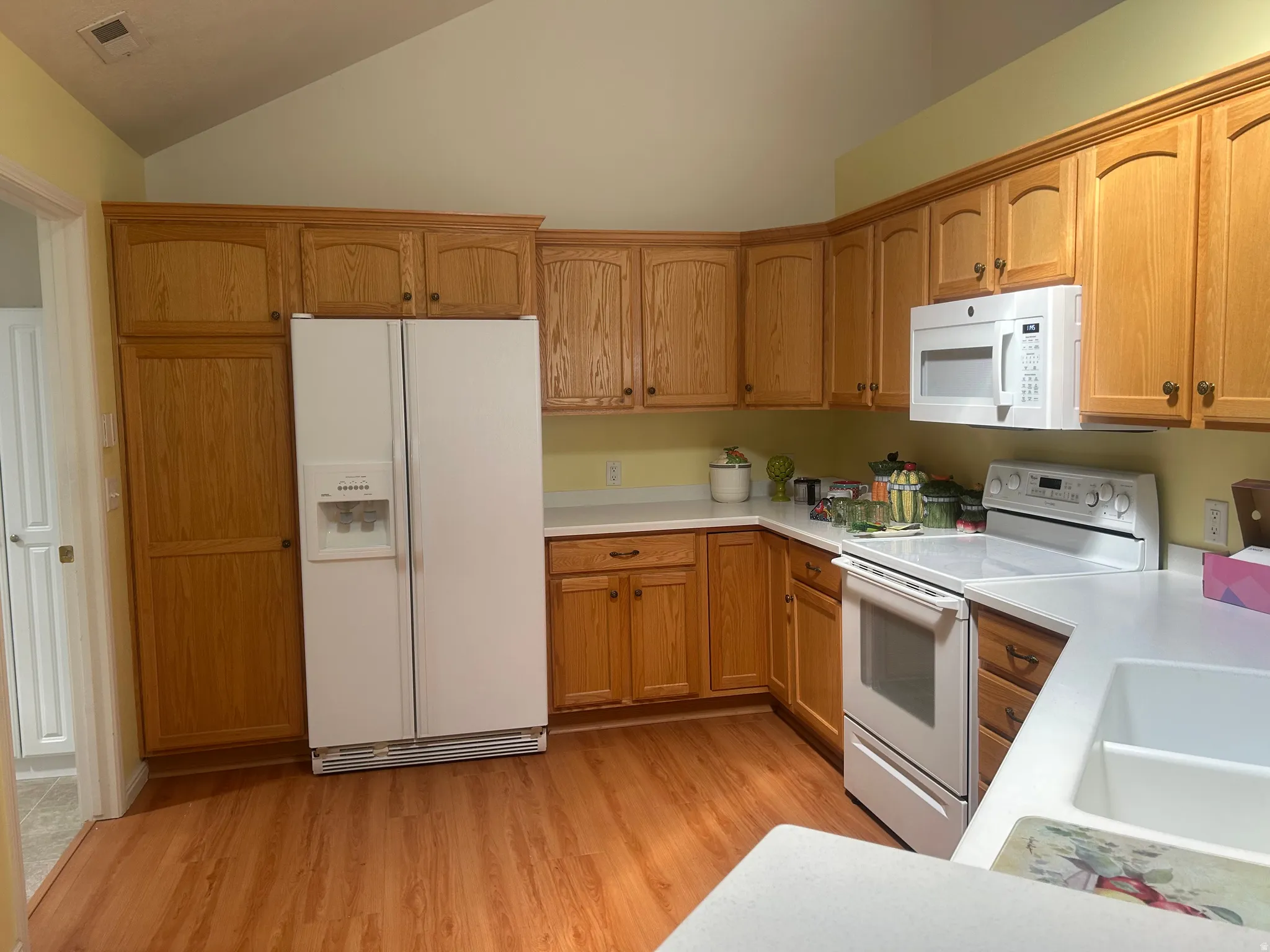 Kitchen featuring wood-finish flooring, wood cabinetry with crown molding, white countertops, and a full suite of white appliances including a refrigerator with ice/water dispenser, range, and built-in microwave