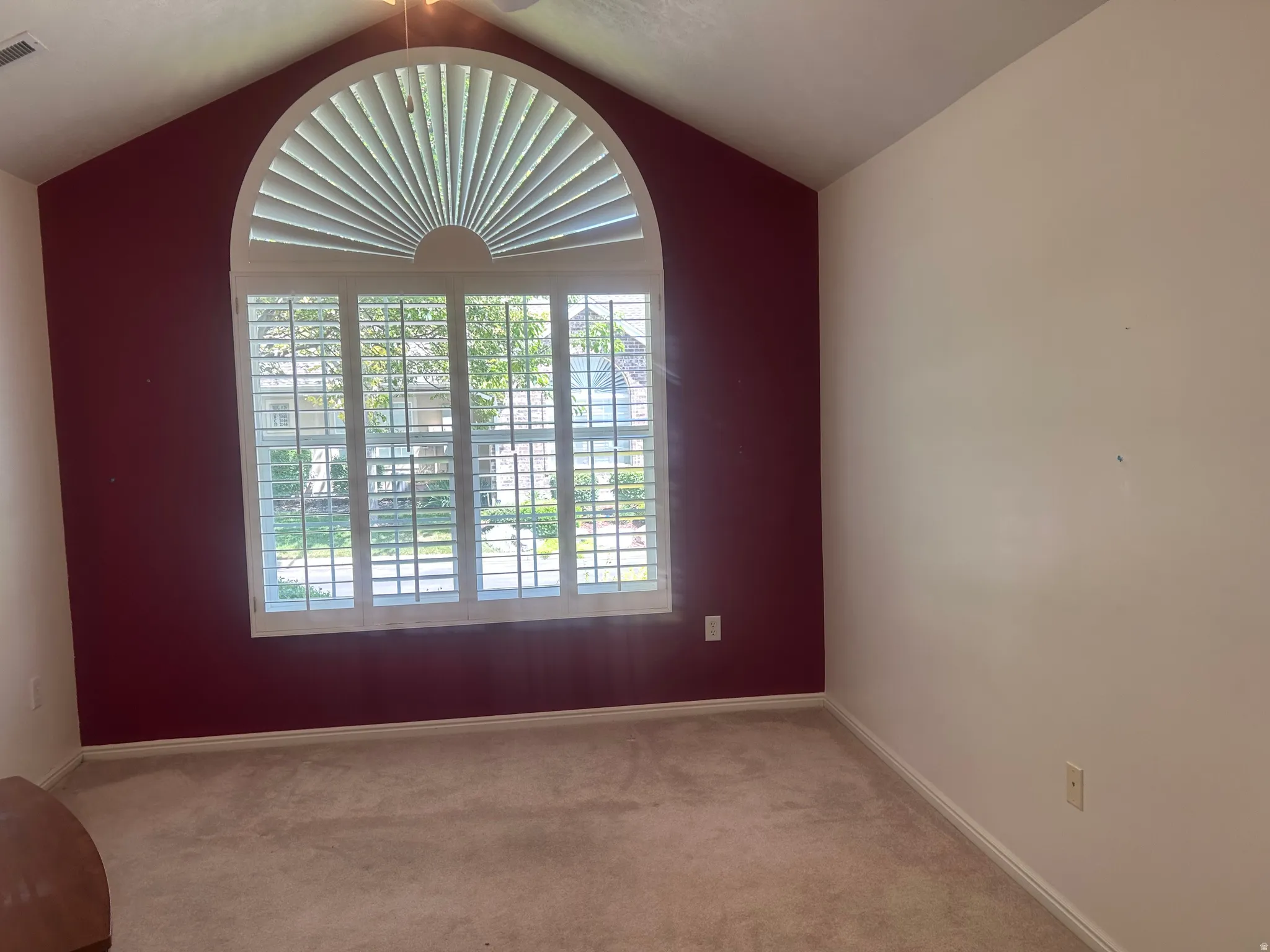 Arch-top window with plantation shutters, vaulted ceiling, and carpeted flooring