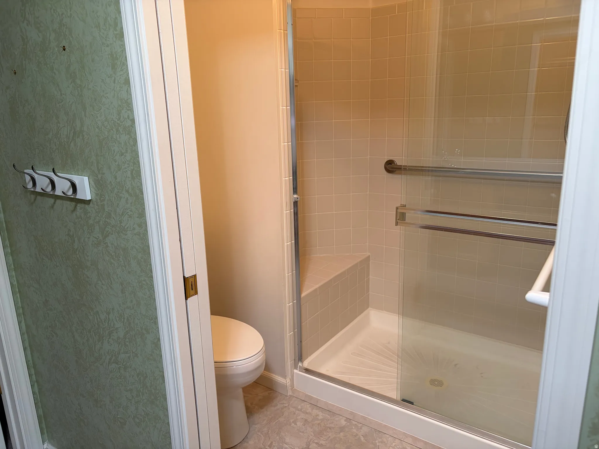 Primary Bathroom glass-enclosed shower with a tiled bench, chrome grab bar, and neutral floor tile