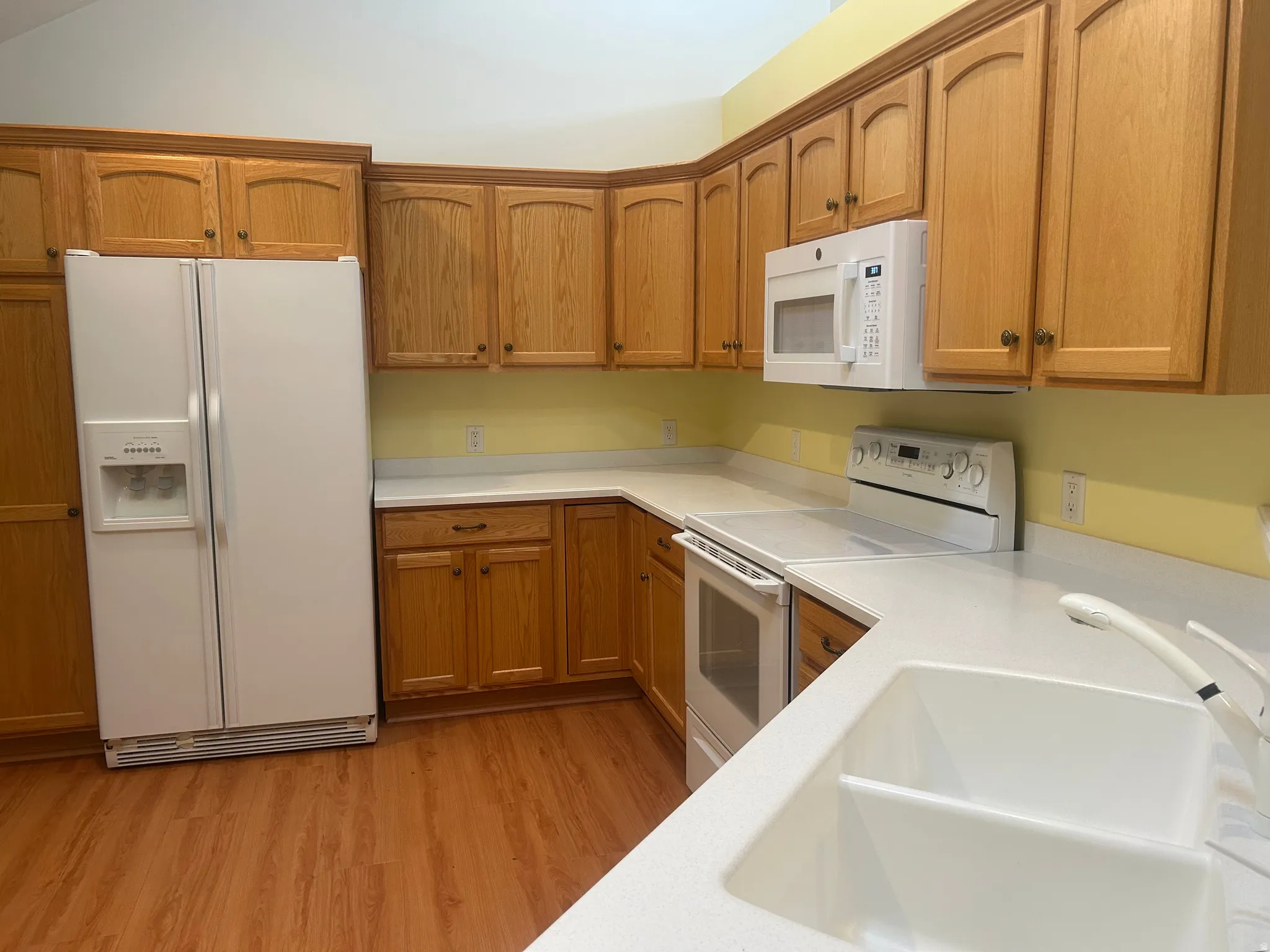 Kitchen featuring wood-finish cabinetry, white appliances, solid surface countertops, and wood-finish flooring