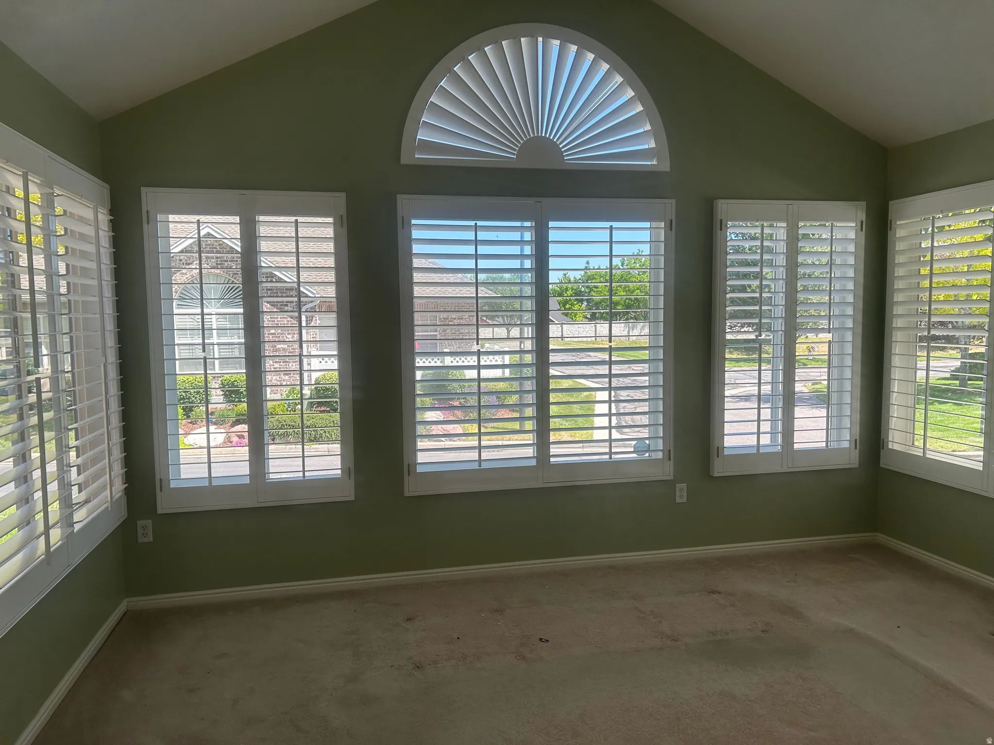 Vaulted ceiling room featuring multiple windows with louvered shutters and a half-round transom window