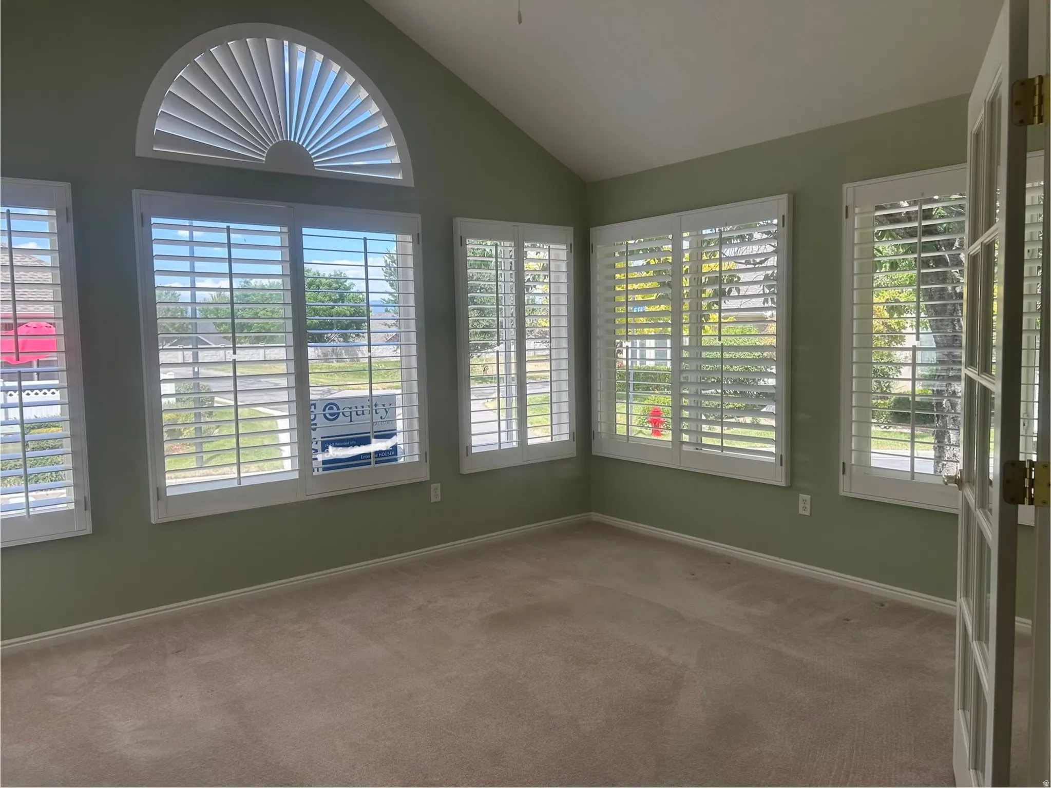 Vaulted ceiling room featuring multiple windows with plantation shutters, including a half-round window