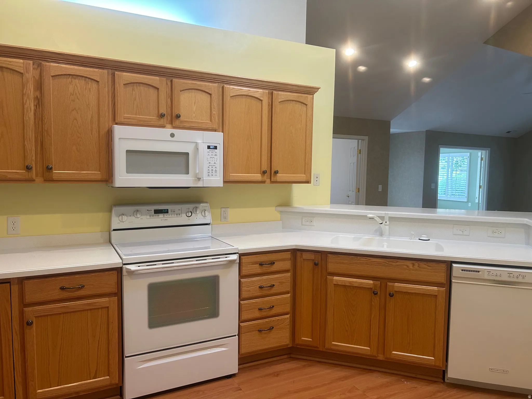 Kitchen featuring light wood cabinetry, white countertops, white range, white microwave, and white dishwasher
