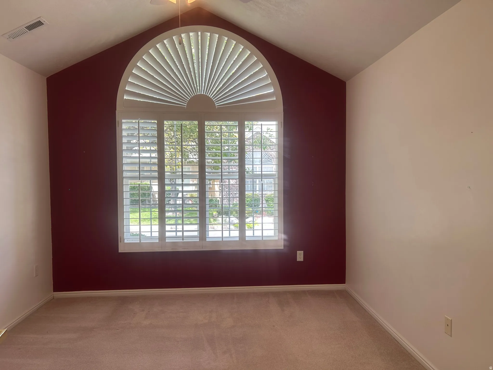 Arched window with plantation shutters, vaulted ceiling, ceiling fan, and neutral carpeting