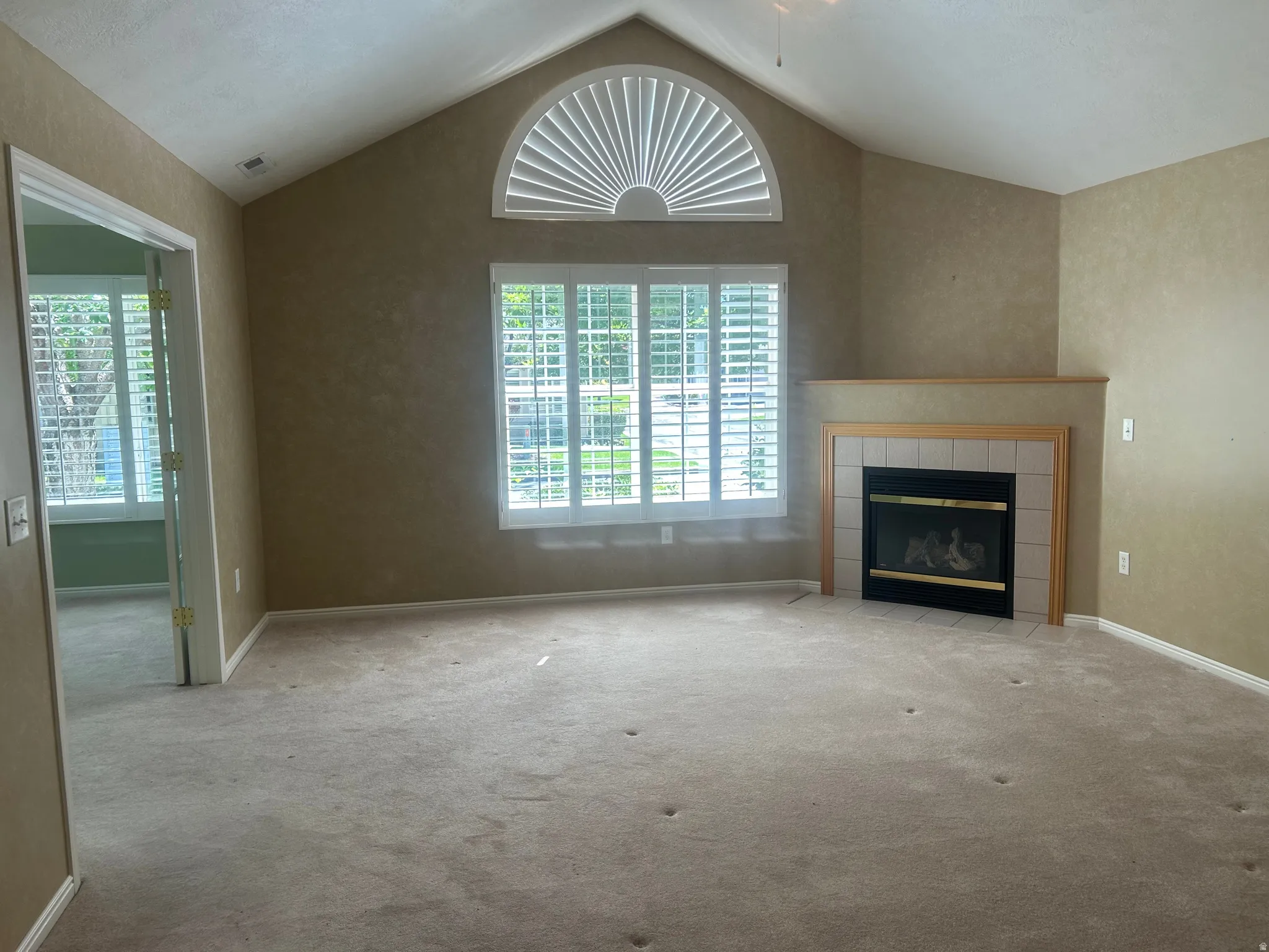 Spacious living area featuring a vaulted ceiling and a prominent fireplace with a tiled hearth and wood mantel