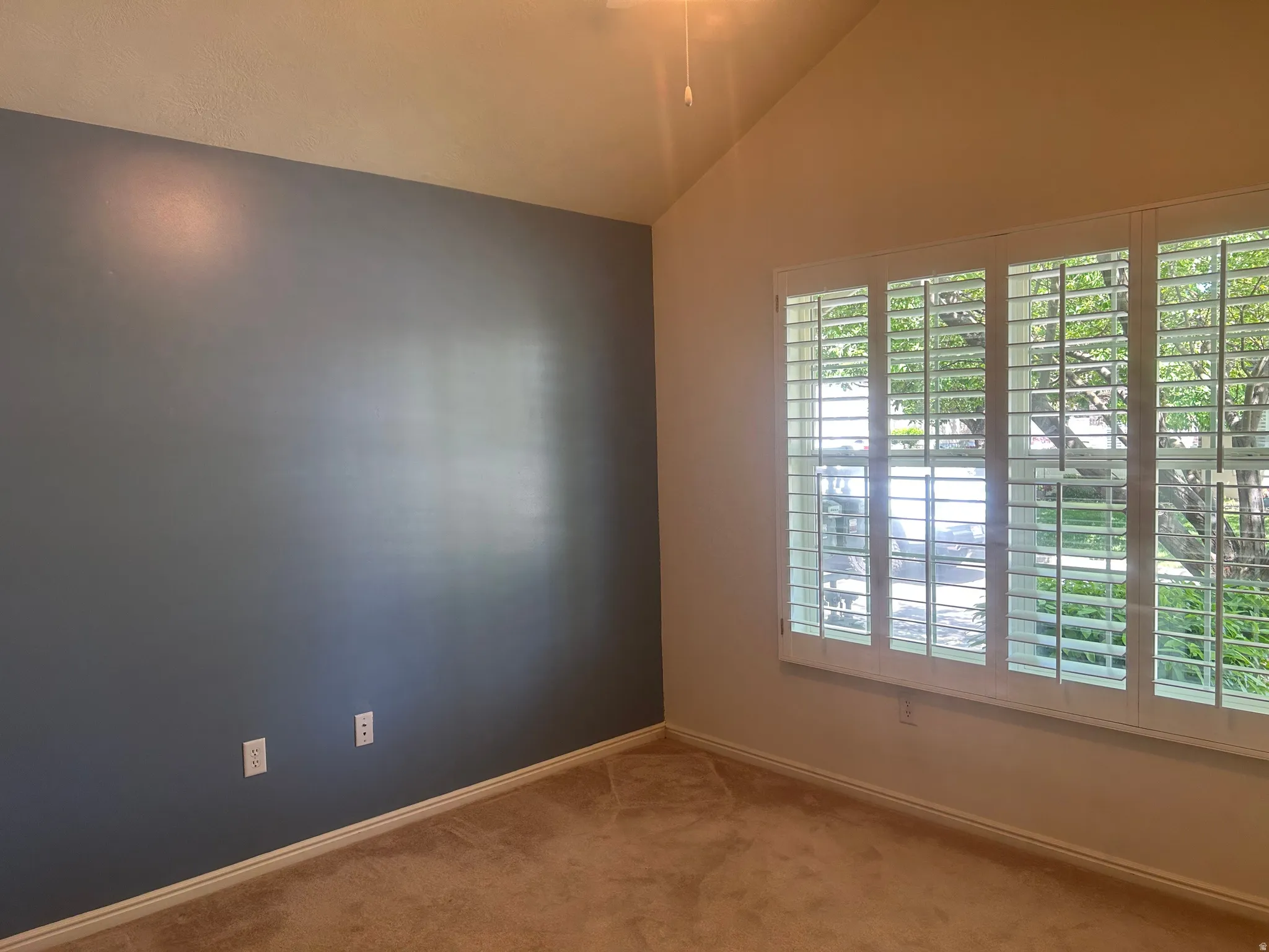 Guest bedroom featuring vaulted ceilings, plantation shutters, and carpet flooring