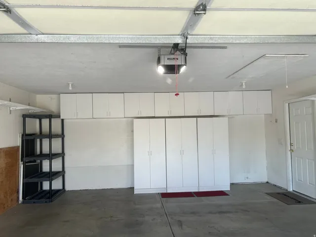 Garage with concrete flooring, overhead cabinetry, full-height storage cabinets, and a white interior door