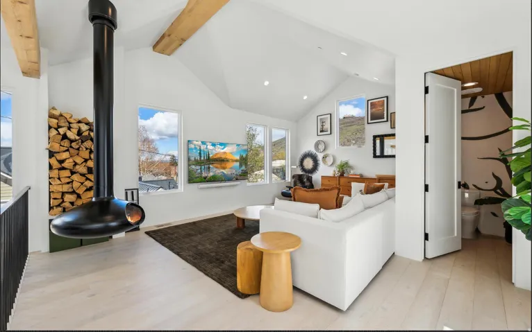 Vaulted ceiling living space featuring a suspended modern fireplace, exposed wood beams, light wood-finish flooring, and multiple windows
