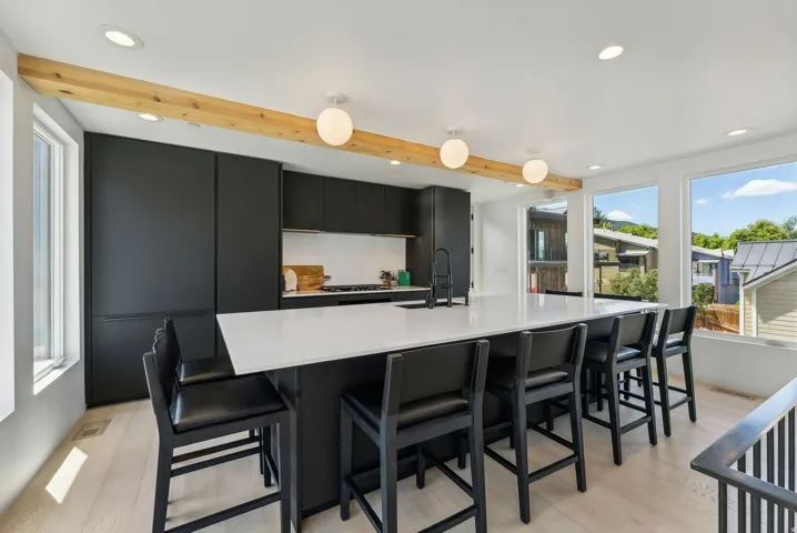 Contemporary kitchen featuring an expansive island with a white countertop and built-in sink, integrated black cabinetry, light wood-finish flooring, and multiple recessed and pendant light fixtures