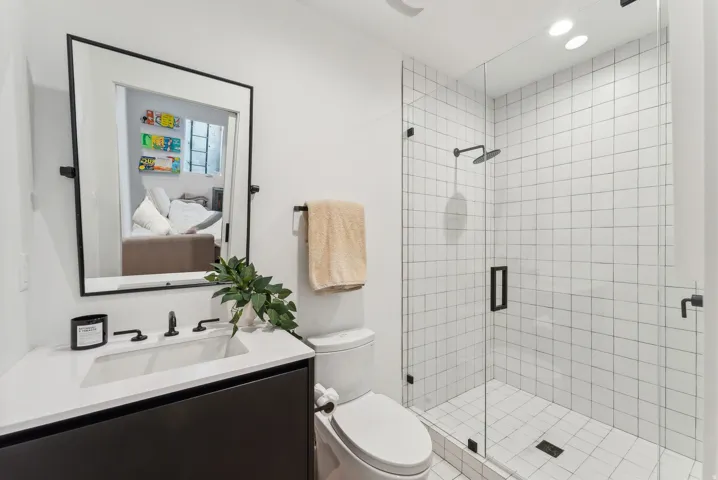 Modern bathroom featuring a frameless glass shower enclosure with matte black hardware and white grid-patterned wall tiles