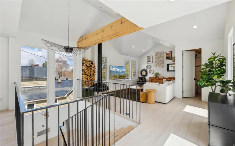 Vaulted ceilings featuring exposed wood beams, a modern pendant light fixture, and light wood-finish flooring