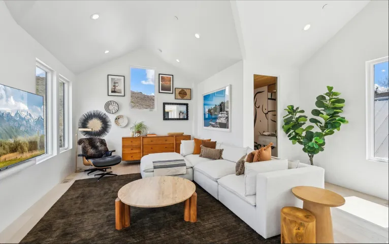 Bright living area featuring vaulted ceilings with recessed lighting, light wood-finish flooring, and multiple windows
