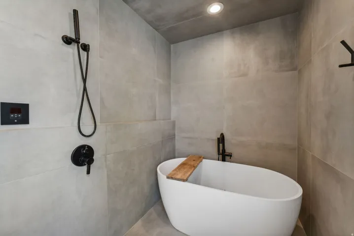 Freestanding soaking tub with matte black fixtures, surrounded by large format tile walls and flooring